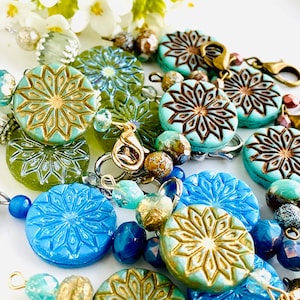 May include: A close-up of a colorful beaded necklace with turquoise and blue patterned beads, gold accents, and silver clasps.