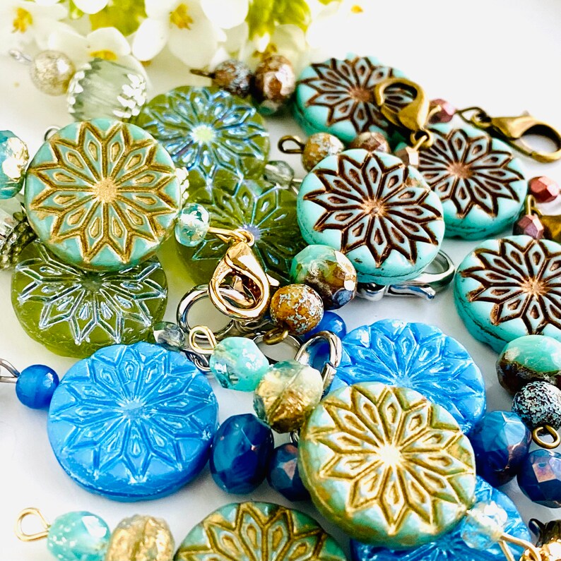 May include: A close-up of a colorful beaded necklace with turquoise and blue patterned beads, gold accents, and silver clasps.
