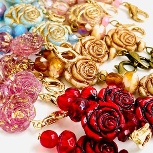 May include: A collection of colorful glass and ceramic rose beads with gold accents. The beads are strung on gold chains with clasps. The beads are a mix of pink, blue, red, and white.