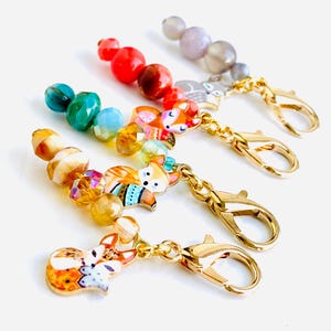 May include: Four colourful beaded fox charms with gold lobster clasps. Each charm features a different colour scheme and a fox with a unique design.