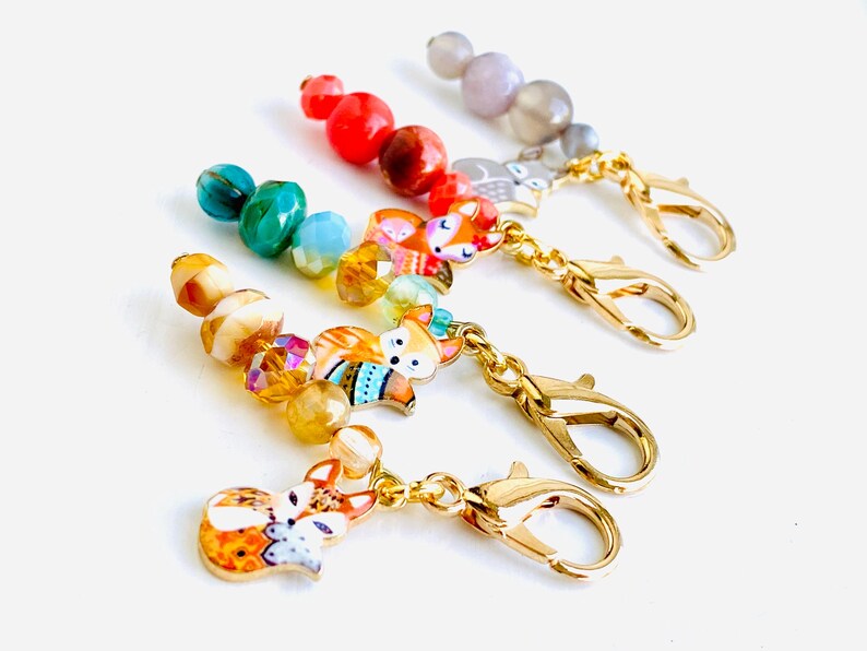 May include: Four colourful beaded fox charms with gold lobster clasps. Each charm features a different colour scheme and a fox with a unique design.