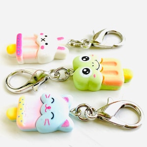 May include: Three colorful popsicle charms with bunny, frog, and cat faces. Each charm has a silver lobster clasp attached.