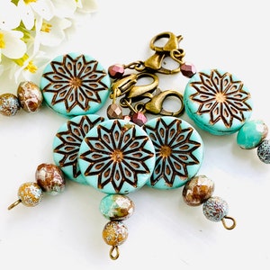 May include: Five turquoise blue and brown patterned beads with gold accents and a gold metal clasp. The beads are strung on a cord and have a decorative design.