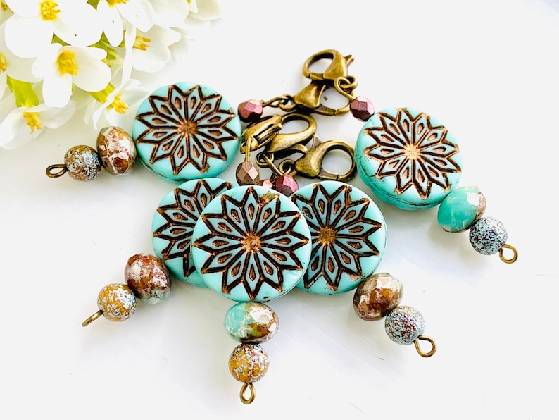 May include: Five turquoise blue and brown patterned beads with gold accents and a gold metal clasp. The beads are strung on a cord and have a decorative design.