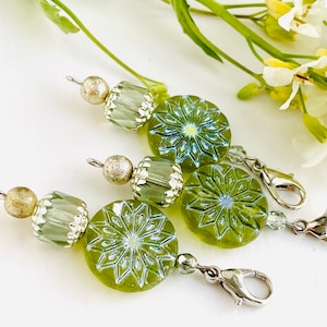 May include: Three green glass bead charms with silver accents and a snowflake design. Each charm has a silver lobster clasp.