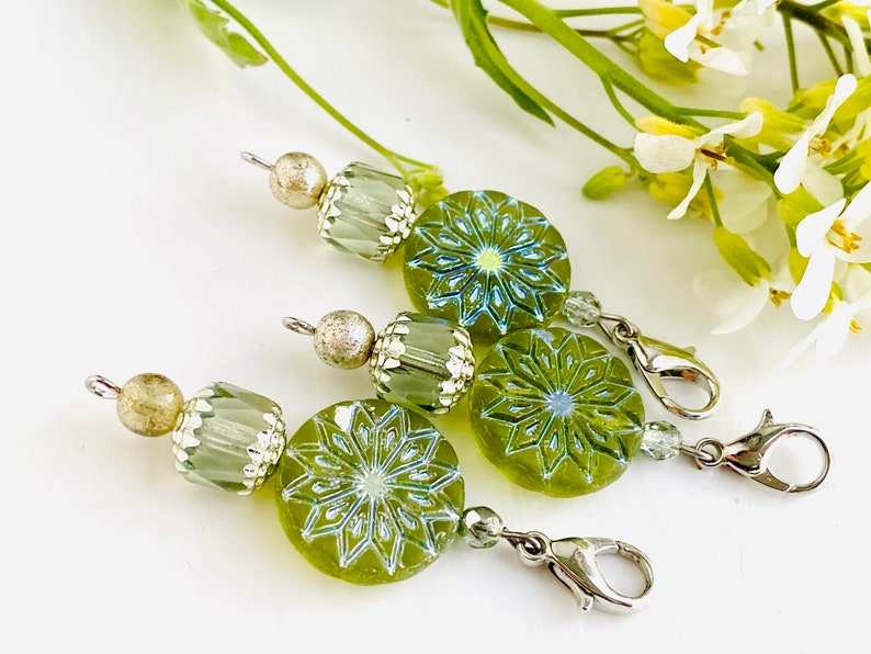May include: Three green glass bead charms with silver accents and a snowflake design. Each charm has a silver lobster clasp.