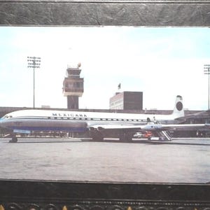 May include: Vintage photograph of a Mexicana Airlines jet on the tarmac. The aircraft is white with a blue stripe and the word "MEXICANA" is printed on the side. The background includes a control tower and a building.