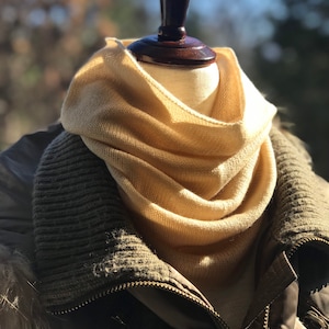 May include: A beige knitted scarf draped over a mannequin, with a brown jacket underneath.