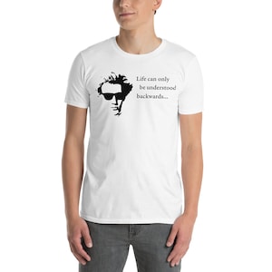 May include: White t-shirt with a black silhouette of a man wearing sunglasses and the text "Life can only be understood backwards..."