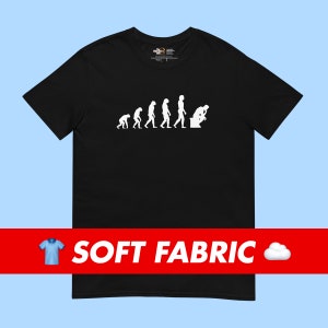 Può includere: Maglietta nera con una grafica bianca dell'evoluzione dell'uomo, che termina con un uomo seduto sul water. Il testo "SOFT FABRIC" è stampato in bianco su uno striscione rosso nella parte inferiore dell'immagine.