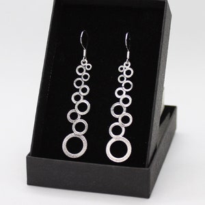 May include: A pair of silver dangle earrings with a cascading design of circles. The earrings are displayed in a black box.