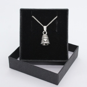 Puede incluir: Un collar con un colgante de dedal de plata con un diseño de corazón, presentado en una caja de terciopelo negro.