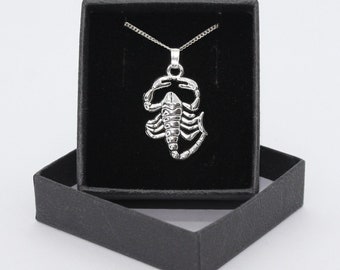 Puede incluir: Un collar con un colgante de escorpión de plata en una caja de terciopelo negro. El escorpión es detallado y tiene un diseño realista.