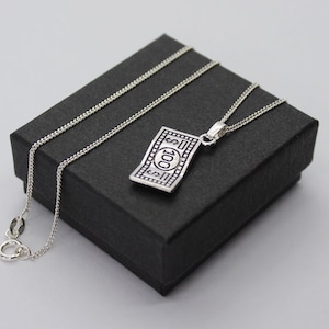 May include: A silver chain necklace with a silver pendant shaped like a $100 bill. The necklace is in a black box.