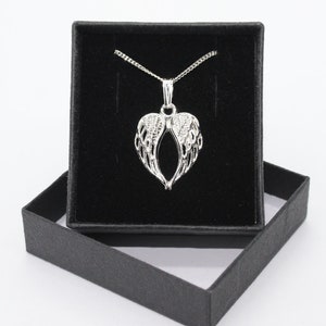 May include: A silver necklace with a heart-shaped pendant featuring angel wings. The necklace is displayed in a black velvet jewelry box.