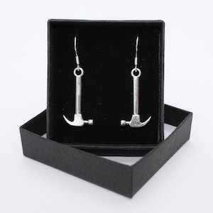 May include: A pair of silver hammer earrings in a black box. The earrings are dangle style and feature a small hammer charm.