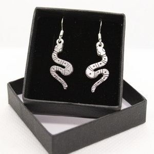 May include: A pair of silver snake earrings in a black jewelry box. The earrings are dangle style and feature a detailed snake design.