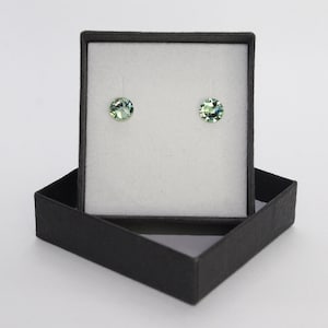 May include: A pair of green crystal earrings in a black gift box. The earrings are round and have a faceted design.