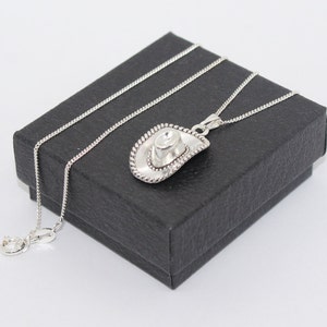 Puede incluir: Un collar de cadena de plata con un colgante de sombrero de vaquero de plata. El collar está en una caja de regalo negra.
