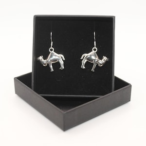 May include: A pair of silver camel earrings in a black jewellery box. The earrings are dangle style with a camel charm.