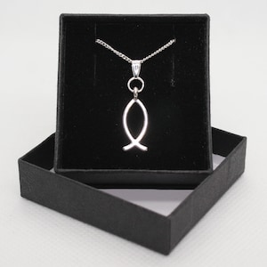 Puede incluir: Un collar de cadena de plata con un colgante de pez de plata en una caja de joyería de terciopelo negro.