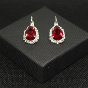 May include: A pair of silver teardrop earrings with a red crystal center and a clear crystal halo.