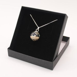 May include: A silver chain necklace with a clear glass orb pendant containing sand and small shells. The necklace is displayed in a black velvet box.
