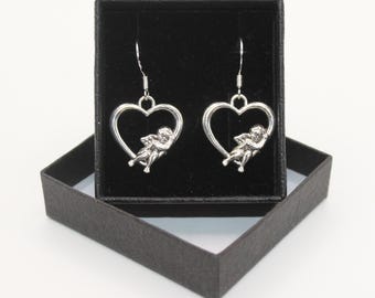 Puede incluir: Un par de pendientes de plata con un diseño en forma de corazón que presenta un querubín dentro de cada corazón.