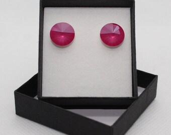 Puede incluir: Un par de pendientes de cristal rosa en una caja de regalo negra. Los pendientes son redondos y tienen un diseño facetado.