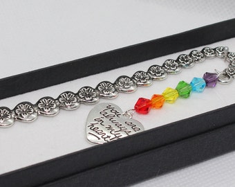 Puede incluir: Un marcapáginas plateado con una cadena de corazones y un encanto de cristal arcoíris. El encanto tiene un corazón plateado con la inscripción "You are always in my heart".