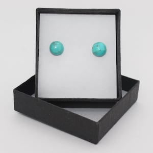 May include: A pair of turquoise stud earrings in a black gift box. The earrings are round and have a smooth, polished finish.