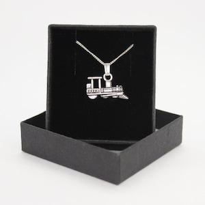 May include: A silver train pendant necklace in a black velvet box. The train pendant is detailed with a chimney, wheels, and a caboose.