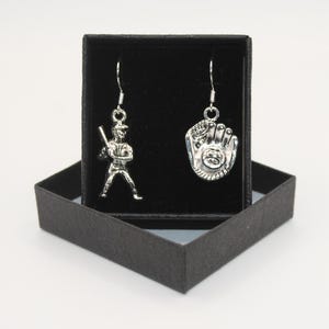 May include: A pair of silver earrings with a baseball player and a baseball glove charm. The earrings are displayed in a black velvet box.