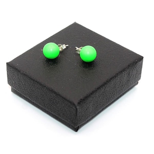 May include: A pair of bright neon green spherical stud earrings with silver-toned metal posts and butterfly backings, resting on top of a square black textured jewelry gift box with a matte finish and a hinged lid design.