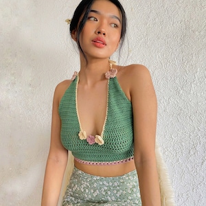 Puede incluir: Un top halter de crochet verde con un dise&ntilde;o floral. El top tiene un escote en V profundo y un ribete de crochet. El top se combina con una falda de estampado floral.