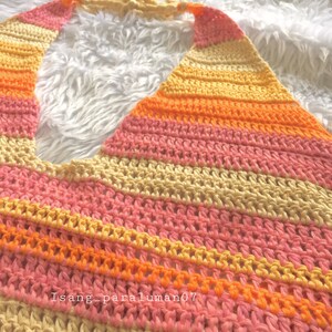 Puede incluir: Un top halter tejido a crochet con un patr&oacute;n de rayas en tonos rosa, naranja y amarillo.