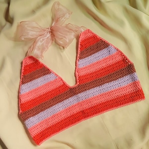 Puede incluir: Un top halter tejido a crochet con rayas rosas, rojas y moradas. El top est&aacute; hecho con un hilo suave y tiene un ajuste holgado.