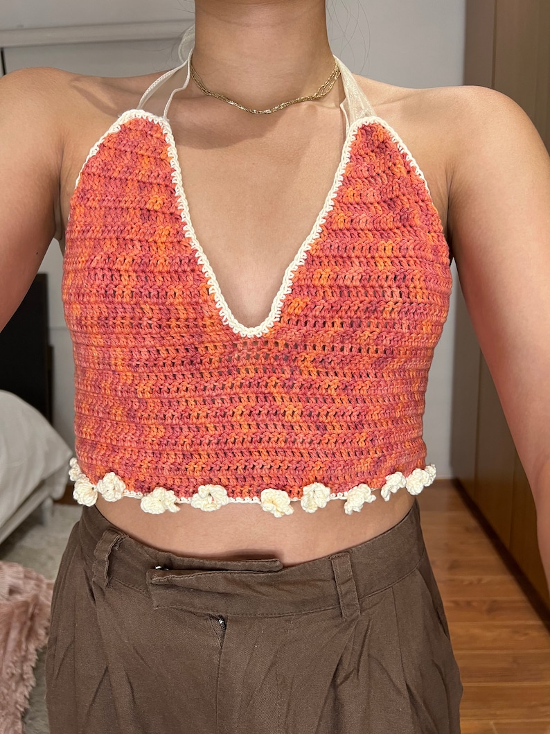 Puede incluir: Un top de halter de ganchillo con un escote en V profundo y un ribete de ganchillo blanco. El top est&aacute; hecho en un esquema de color naranja y rosa brillante y tiene un ribete en forma de flor alrededor de la parte inferior.