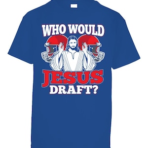 May include: A royal blue t-shirt with a white graphic of Jesus wearing a white robe and holding up his hands. The graphic is surrounded by two red and white football helmets. The text "WHO WOULD JESUS DRAFT?" is printed in white, red, and blue letters.