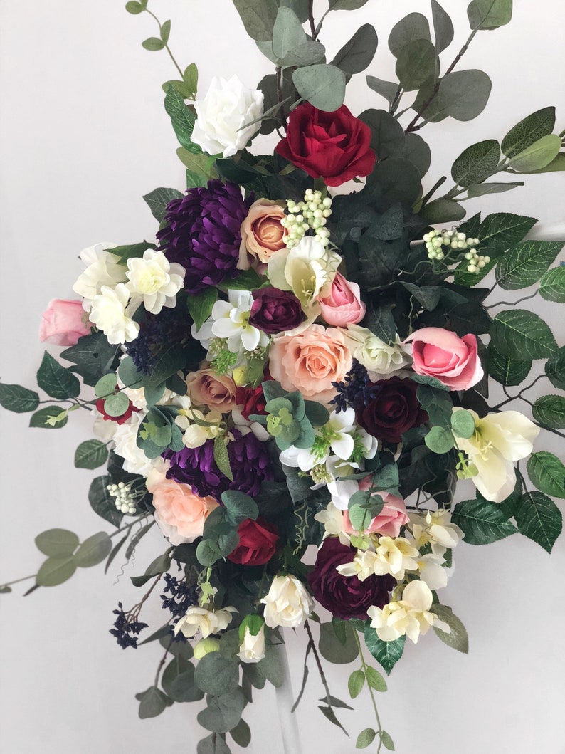 May include: A lush floral arrangement featuring a variety of flowers in shades of pink, red, white, and purple. The arrangement includes roses, hydrangeas, and other blooms, as well as greenery.