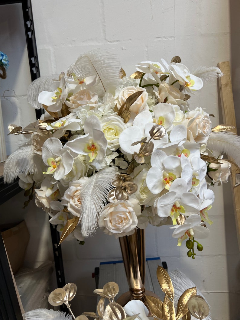 K&ouml;nnte beinhalten: Ein wei&szlig;-goldener Blumenstrau&szlig; mit Orchideen, Rosen und Federn in einer goldenen Vase. Der Strau&szlig; ist perfekt f&uuml;r eine Hochzeit, eine Party oder einen besonderen Anlass.