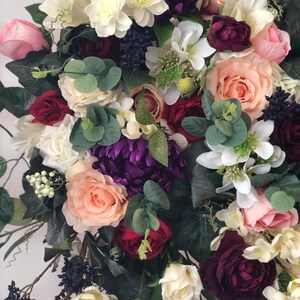 May include: A bouquet of artificial flowers in shades of pink, white, burgundy, and purple. The bouquet includes roses, hydrangeas, and eucalyptus.