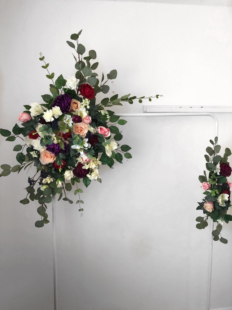 Artificial wedding flower archway swag featuring burgundy roses, plum, peach, and ivory silk flowers with eucalyptus and rose leaves, displayed as a floral arch for boho weddings, ceremony backdrops, or entryway decoration.