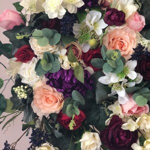 May include: A bouquet of artificial flowers in shades of pink, white, burgundy, and purple. The bouquet features roses, hydrangeas, and greenery.