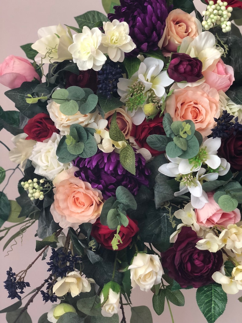 May include: A bouquet of artificial flowers in shades of pink, white, burgundy, and purple. The bouquet features roses, hydrangeas, and greenery.