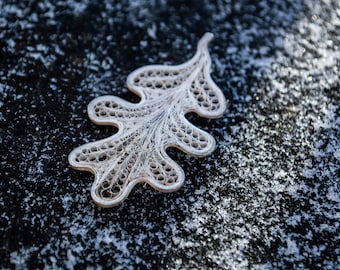 May include: A white paper quilling oak leaf with intricate details, set against a dark background with white flecks.