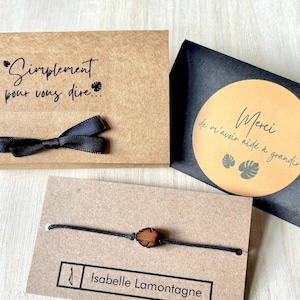 Op de afbeelding: Een bruine papieren cadeaudoos met een zwart lint en de tekst "Simplement pour vous dire..." Een zwarte kaart met een gele cirkel en de tekst "Merci de m'avoir aidé à grandir." Een bruine kaart met een zwart koordarmband met een houten kraal en de tekst "Isabelle Lamontagne".