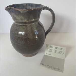 Puede incluir: Una taza de cerámica blanca con un asa negra y el texto "But First, Coffee" en negro, en negrita. La taza está sobre una superficie blanca.