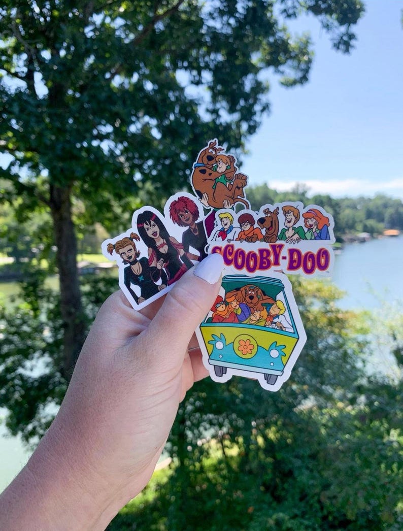 May include: A collection of colorful Scooby-Doo stickers featuring the Mystery Inc. gang and the Mystery Machine van. The stickers showcase various characters and scenes from the animated series, with vibrant colors and detailed designs.