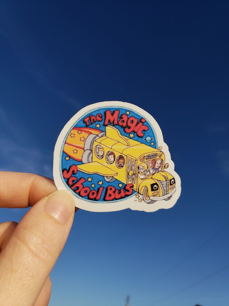 May include: A white sticker with a yellow school bus flying through the air with a rocket attached to the back. The bus is filled with children. The text on the sticker reads "The Magic School Bus".